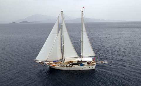Kayhan 3 sailing yacht with white sails on calm blue sea, distant rocky islands