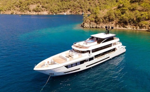 Large white luxury yacht anchored in clear blue water near rocky coastline