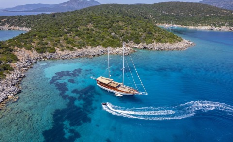 Arabella sailing near turquoise cove with rocky coastline and green hills