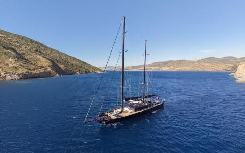 A sleek two-masted sailing yacht gliding in calm blue waters near rocky coastline