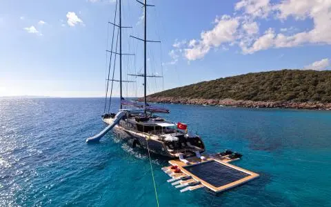 Sunlit open sea with the luxury sailing yacht OGUZ KHAN alongside a floating pool and deck seating