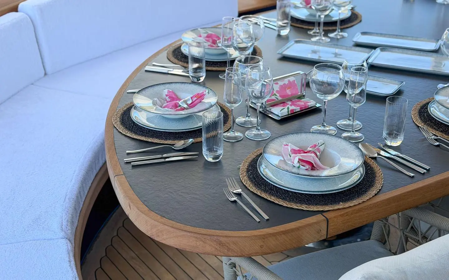 Outdoor yacht dining table set with plates, glasses and floral napkins on a wooden-edged table
