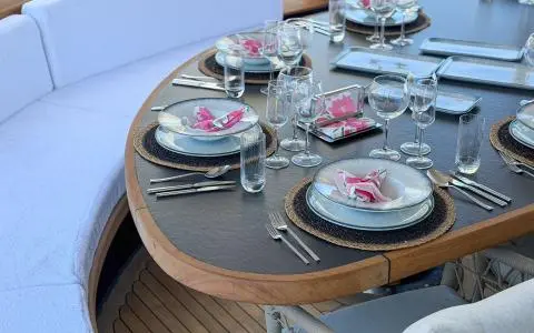 Outdoor yacht dining table set with plates, glasses and floral napkins on a wooden-edged table