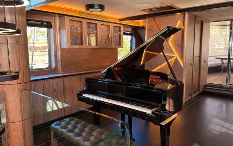 Luxurious yacht interior with a black grand piano open, wooden cabinetry and warm lighting