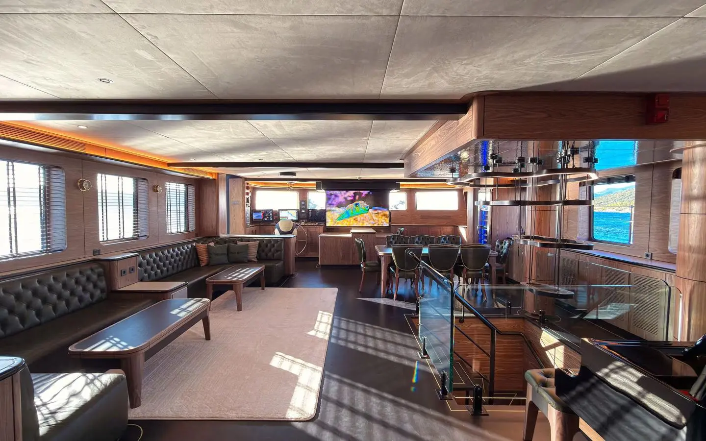 Luxurious yacht interior with a large seating area and conference table, TV screen in the background and windows with exterior view