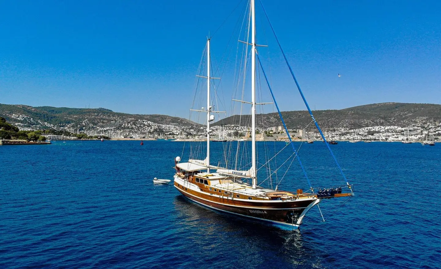 Sailing yacht Enderim A anchored on blue sea with city coastline in background