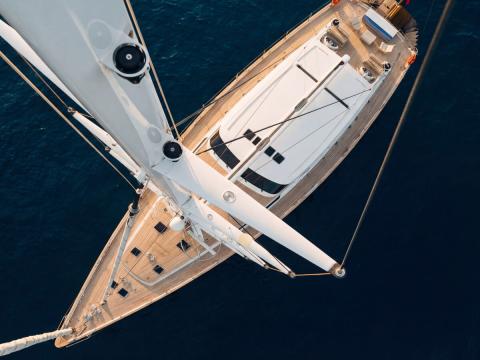 Aerial view of a white luxury sailing yacht with teak deck and mast over dark blue sea