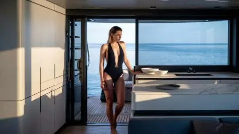 Woman in black swimsuit standing inside yacht by open door with sea view
