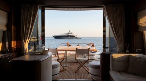 Interior view through open aft deck to a motor yacht anchored offshore with seating and folding chairs