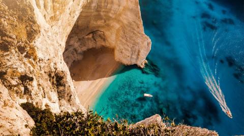 Aerial view of steep limestone cliffs above turquoise sea with a small boat and sandy cove