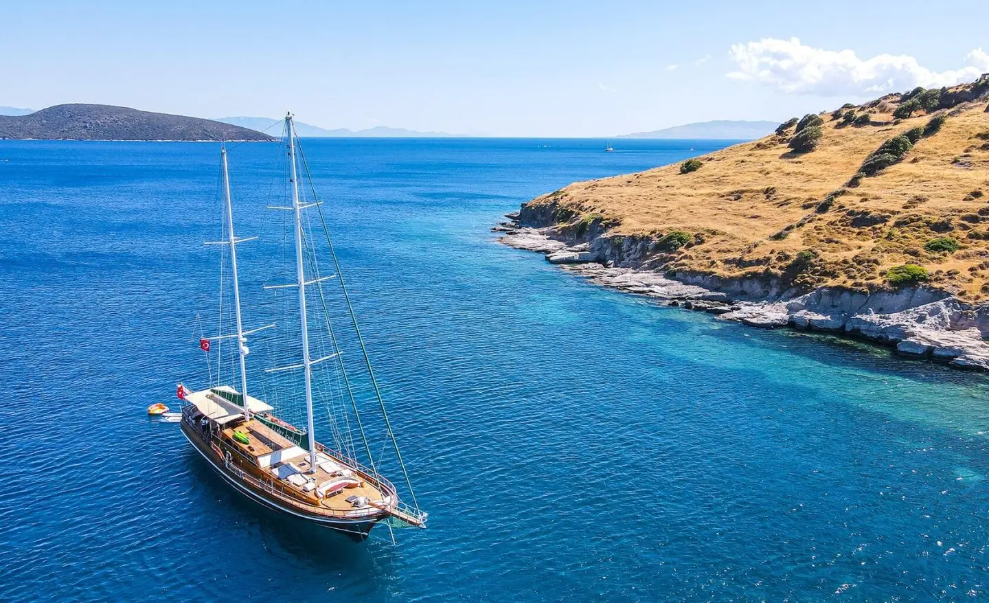 Calm blue sea with a luxury gulet near rocky coastline at sunset