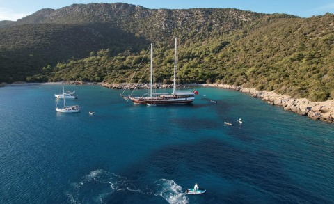 Two-masted gulet anchored in a bay with turquoise water and rocky shoreline