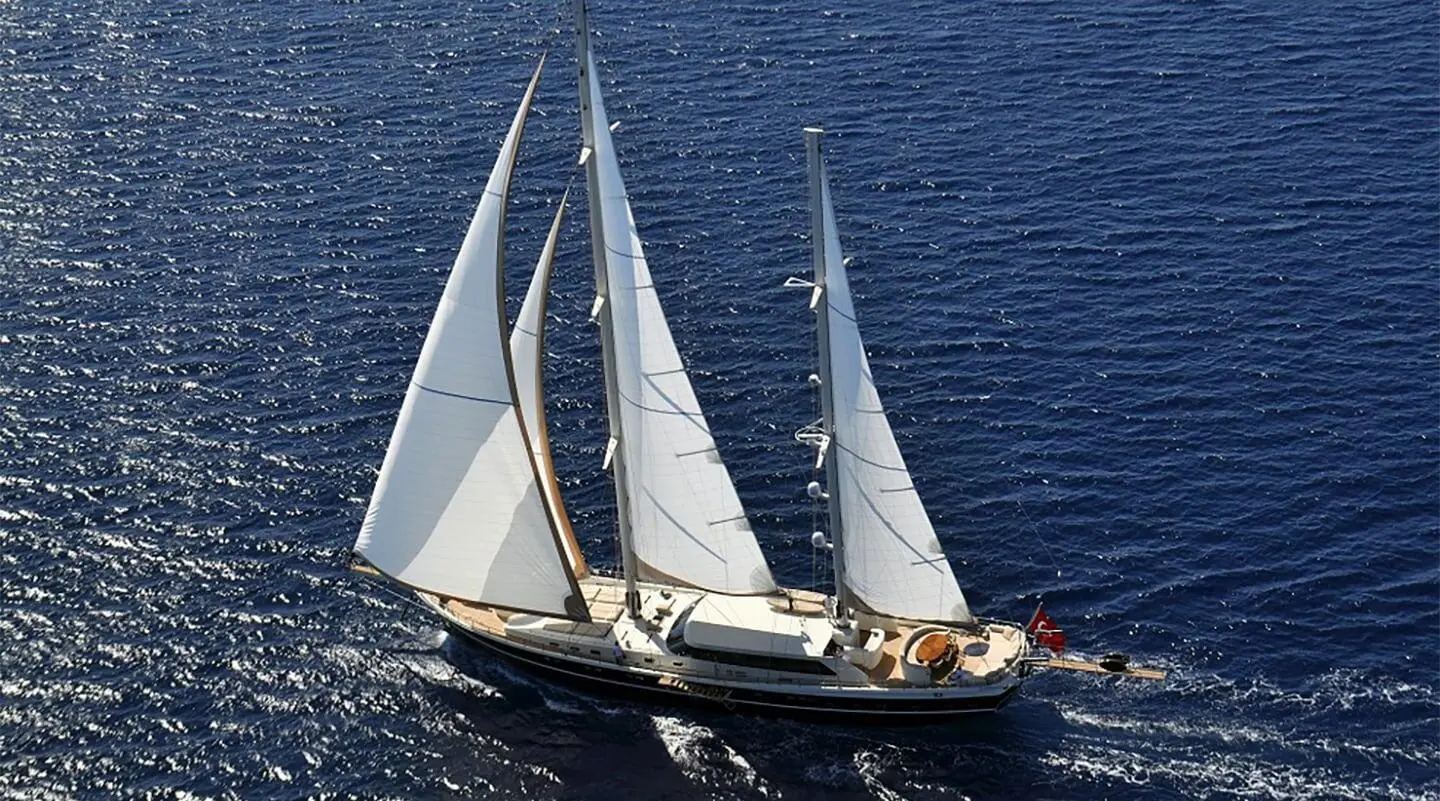 Dolce Mare yacht with sails unfurled on calm blue sea at sunset