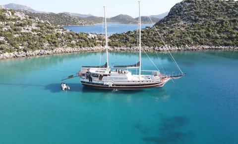 Luxurious sailing gulet yacht anchored in turquoise water near rocky coastline at daylight