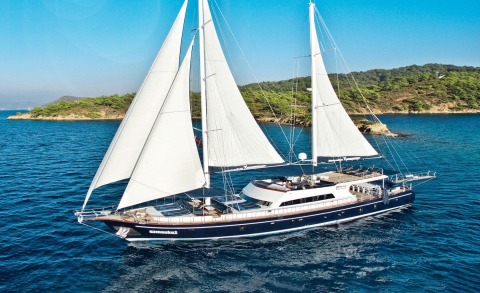 Maske2 yacht with large white sails on blue sea near green coastline