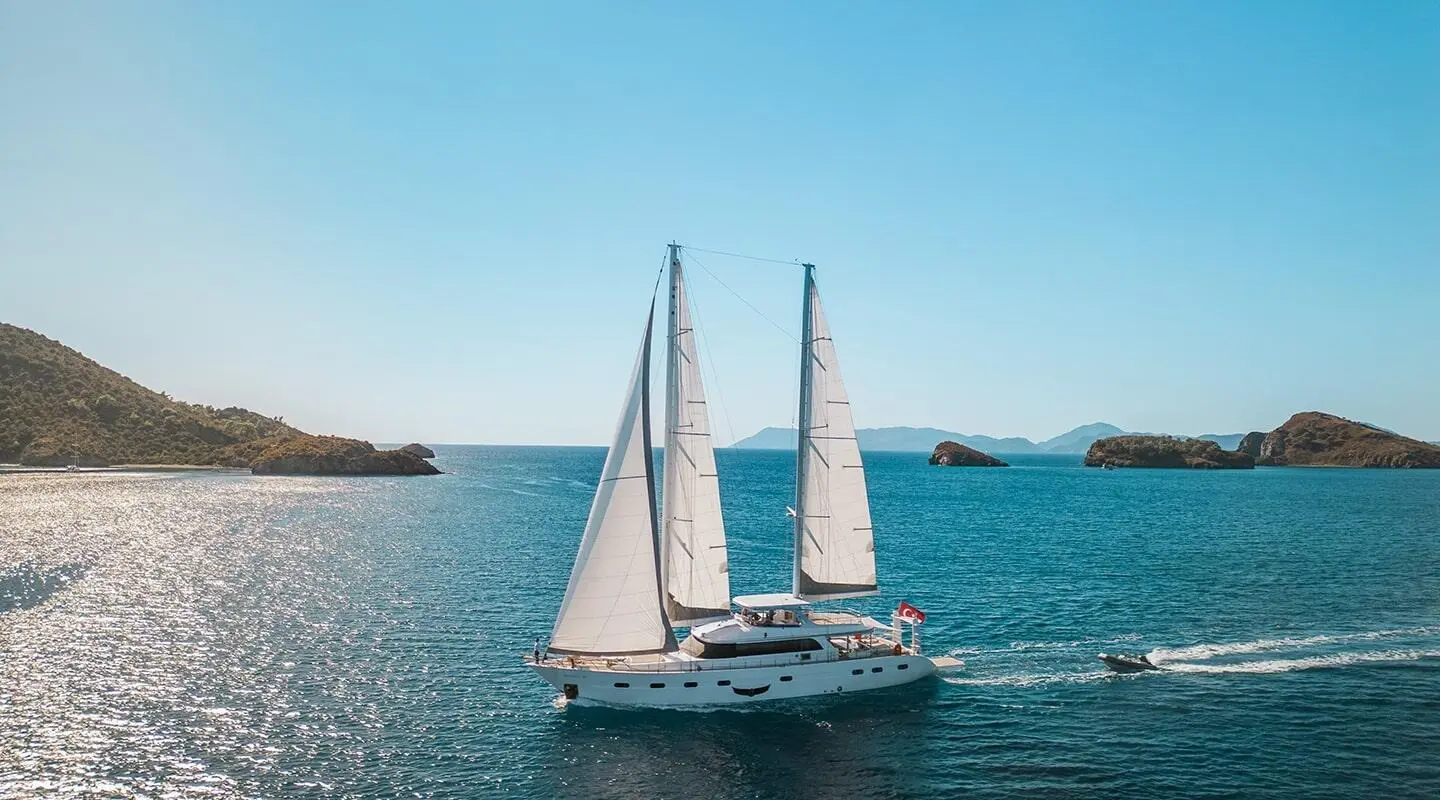 Yacht Angelo III sailing on calm blue water with sails raised at sunset