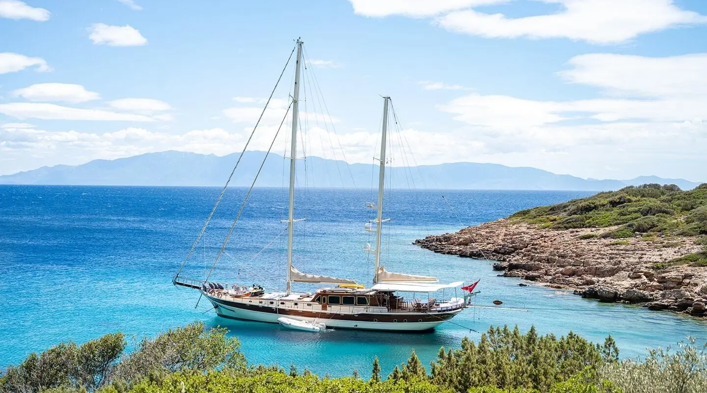 Estrella De Mar yacht anchored in blue bay with cliffs and clear water at sunset