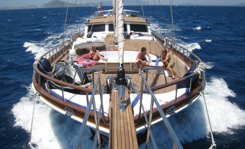 View from the bow of a yacht with several people sunbathing on a wooden deck