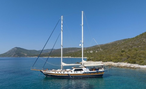 Two-masted sailing yacht Artemis anchored in blue sea near rocky shore