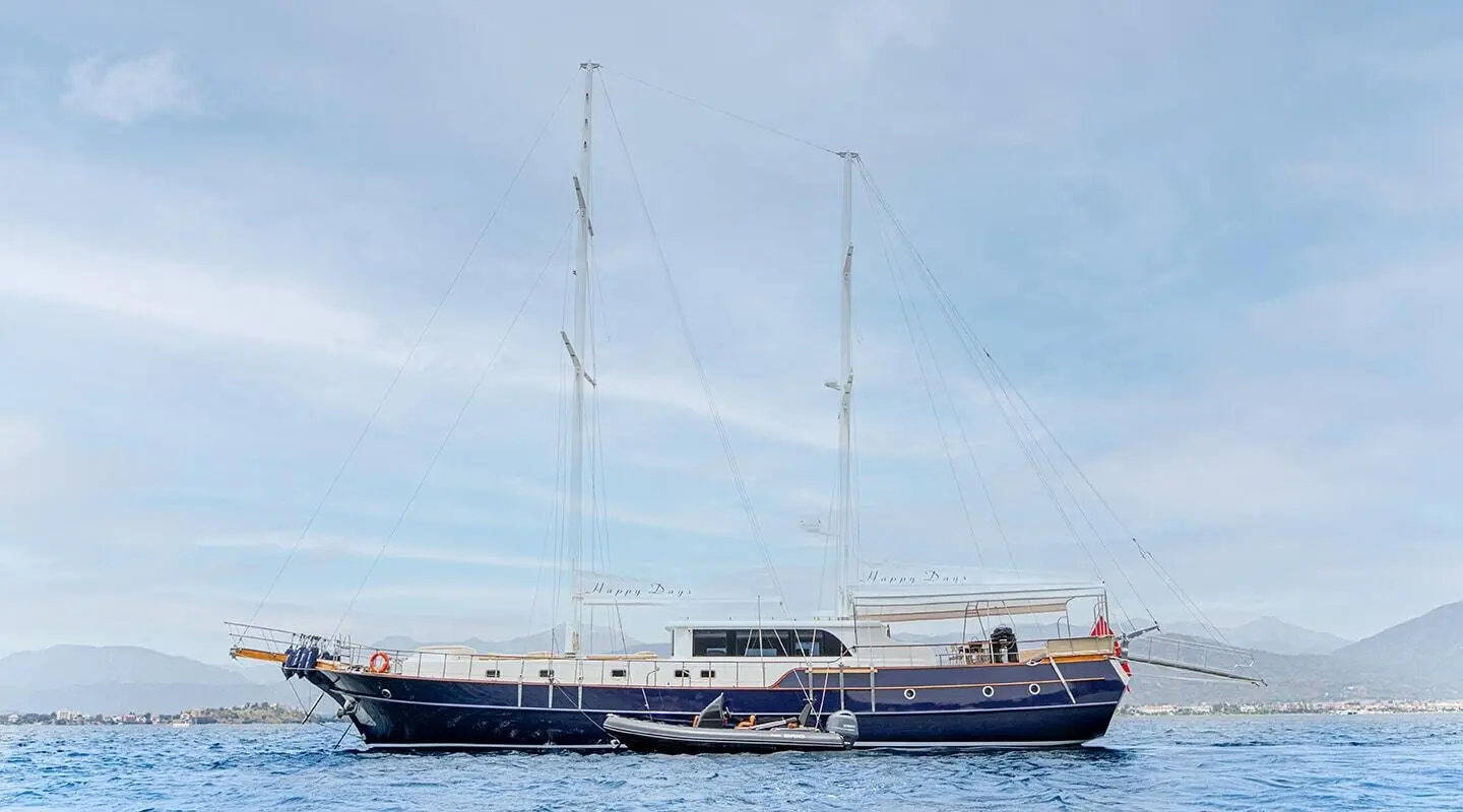 Yacht 'Happy Days' sailing boat with two masts on calm blue water at sunset