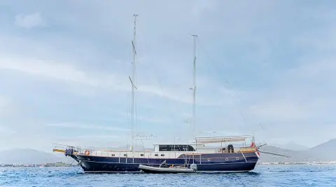 Yacht 'Happy Days' sailing boat with two masts on calm blue water at sunset