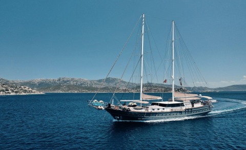 Two-masted luxury sailing yacht on blue sea with distant rocky coastline