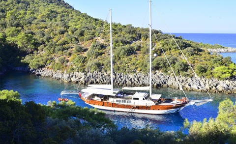 Berrak Su classic 33m sailing yacht anchored in a tranquil turquoise cove amid rocky coastline and pine trees