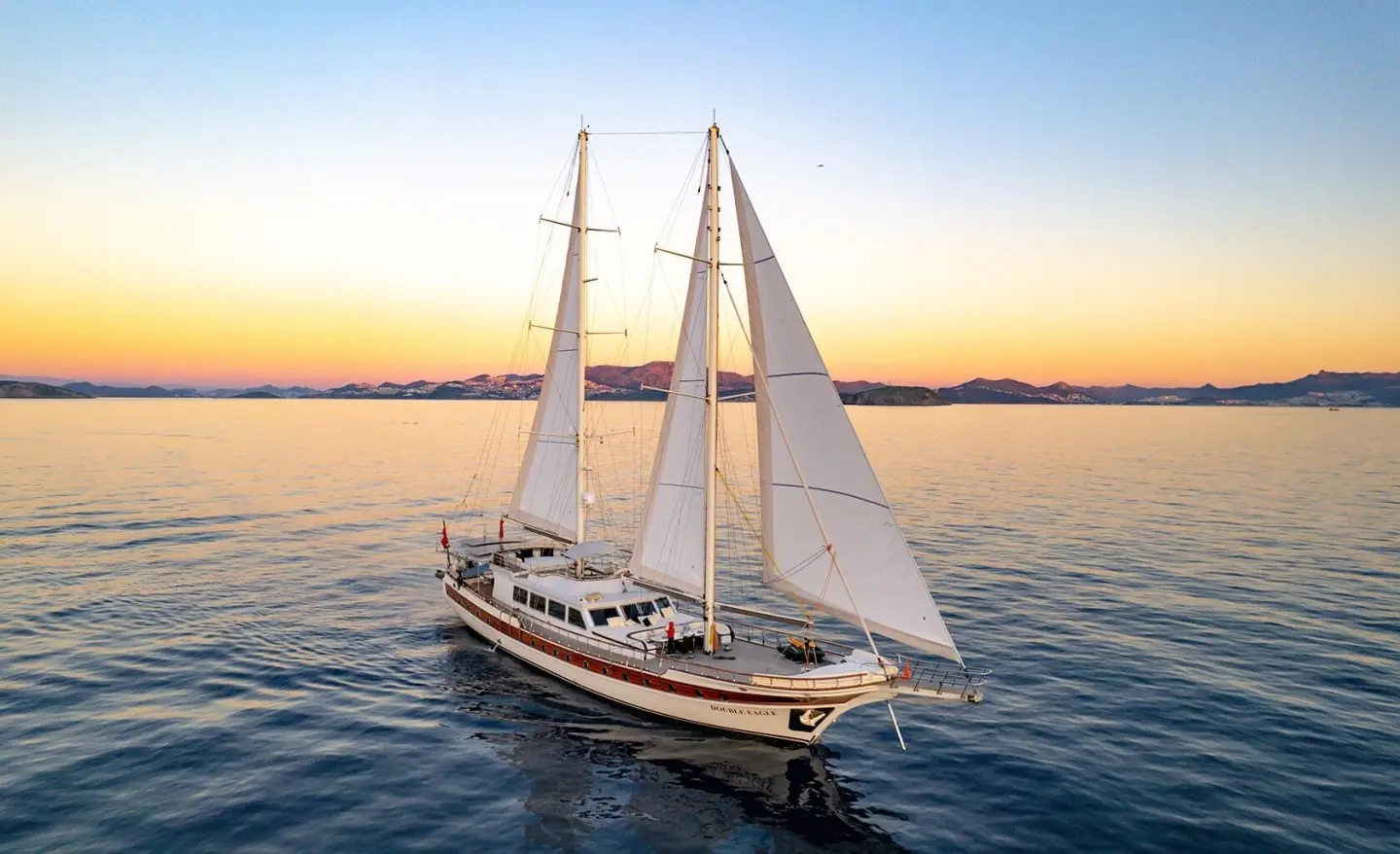Double Eagle luxury yacht sailboat on calm sunset water with sails raised