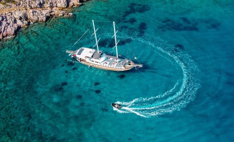 A white Bodrum Queen sailing yacht anchored near rocky coastline in turquoise waters