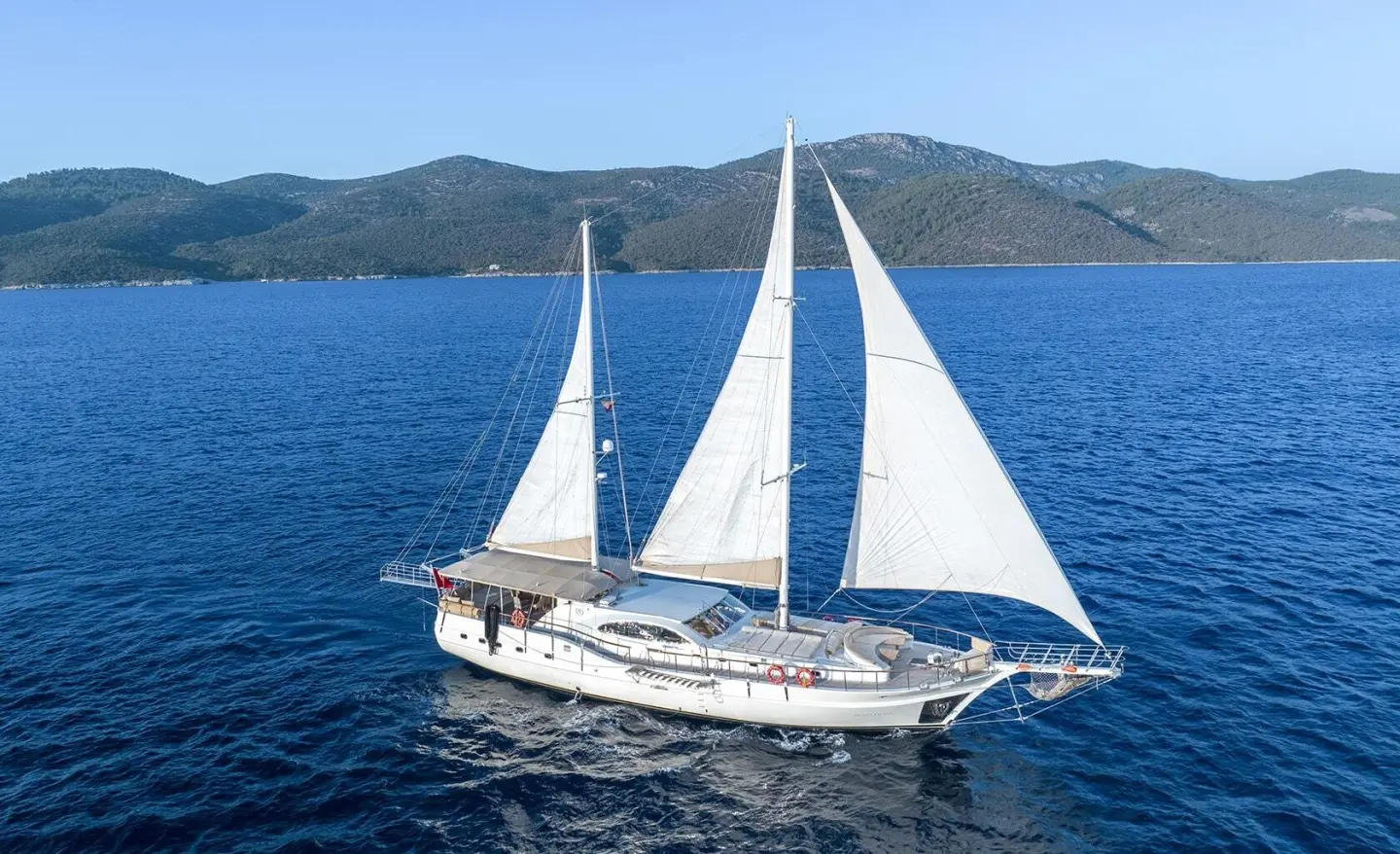 Queen Of Sea yacht with white sails on calm blue waters at sunset