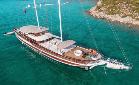 Halcon Del Mar yacht anchored in turquoise waters near rocky coastline, spacious aft deck with sun loungers and seating
