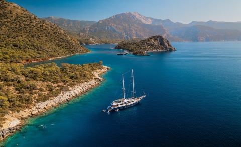 Esma Sultan yacht in open sea with blue water and rocky coastline in view