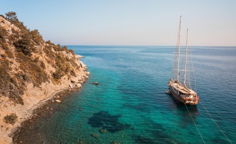 Sailing yacht anchored in turquoise water near rocky coastline