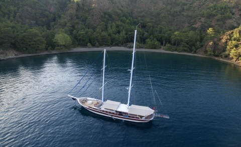 Kayhan Kaptan sailing yacht anchored in a secluded turquoise bay with forested cliffs