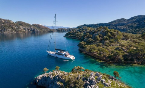 White sailing yacht anchored near rocky coastline with clear blue-green water