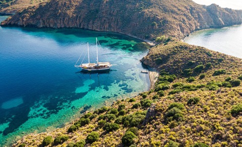 Derin Deniz yacht anchored in turquoise water near rocky coastline with green shrubbery