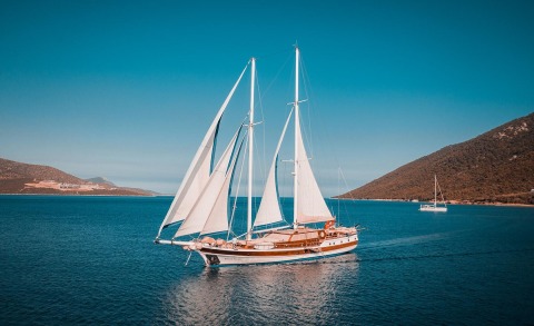 Wicked Felina sailing yacht with white sails on calm blue sea near hilly coastline