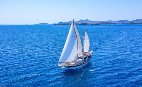 Gantry view of a two-masted gulet yacht sailing on blue sea with white sails