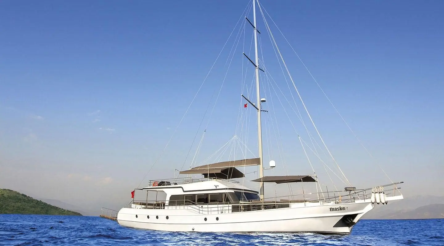 Maske 5 sailing yacht anchored on calm blue water with clear sky and distant hills
