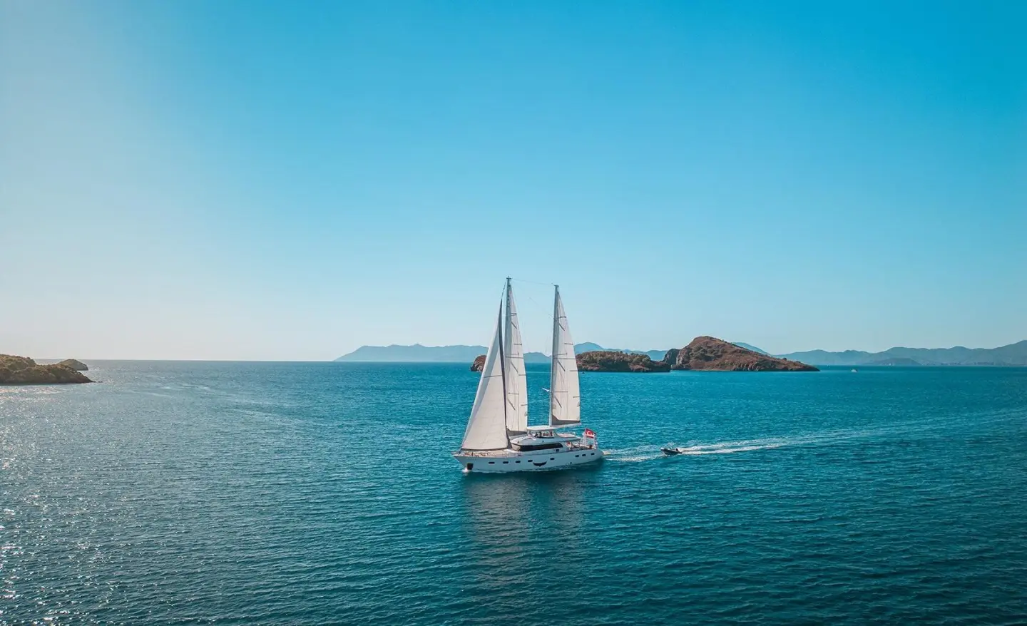 White sailing yacht with two masts on blue sea and distant islands