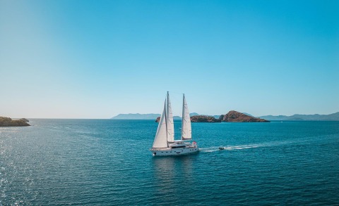 White sailing yacht with two masts on blue sea and distant islands