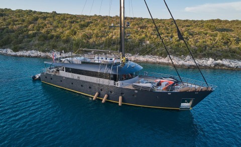 Gulet Rara Avis moored on blue water with rocky shore in background
