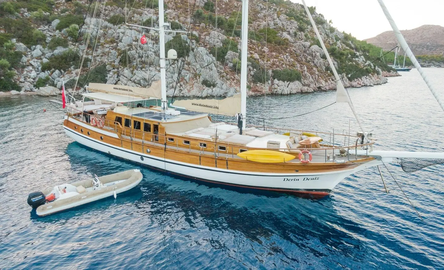 Derin Deniz yacht alongside a wooden luxury gulet at sunset harbor
