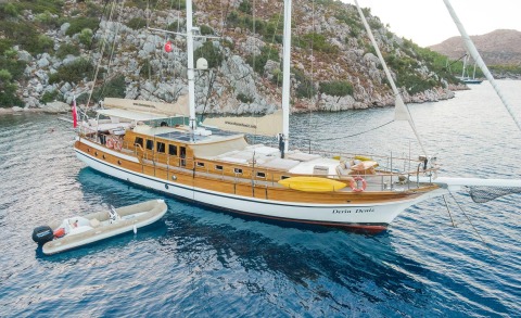 Derin Deniz classic wooden schooner anchored near rocky coastline with small tender beside