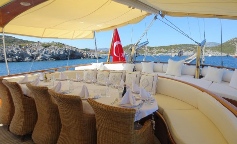 Table set on a yacht deck with white tablecloth and wicker chairs, Turkish flag and blue sea in the background