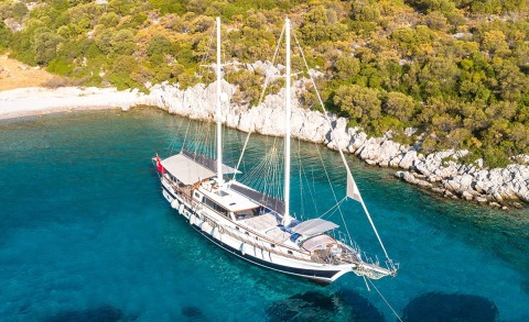Luxurious gulet yacht anchored near rocky shoreline by turquoise water
