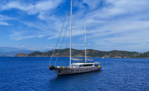 Two-masted yacht anchored on blue sea with hilly coastline in the background