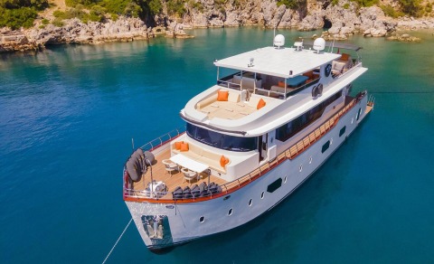 Motor yacht Simay M in turquoise sea, white hull with orange cushions on a spacious deck seating area