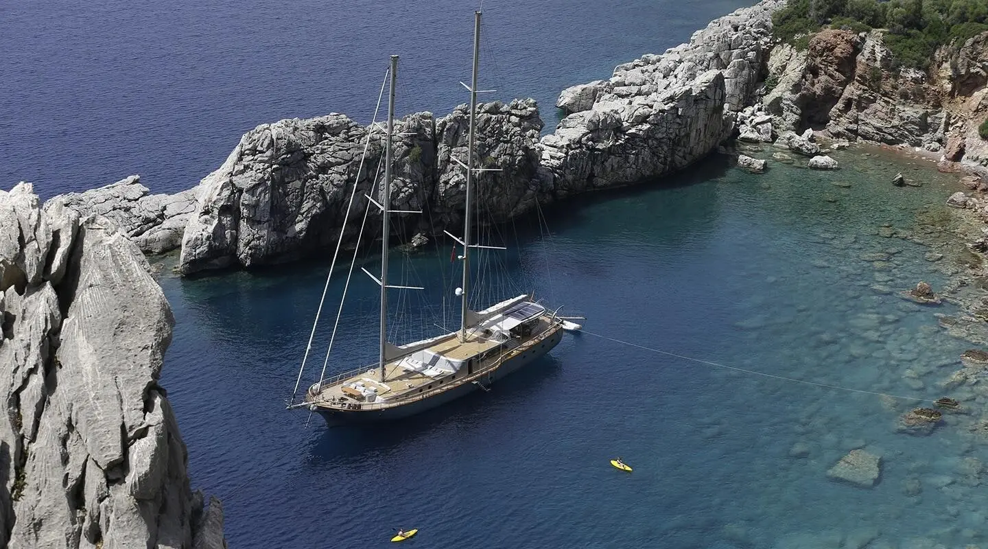 Sailing yacht anchored between rocky cliffs in turquoise water