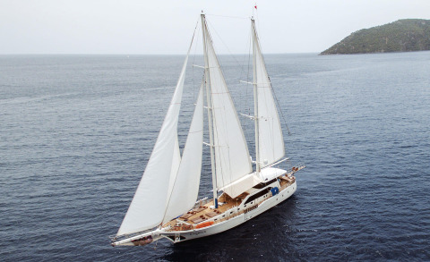 Kayhan 3 sailing yacht with white sails underway on deep blue sea near a green island